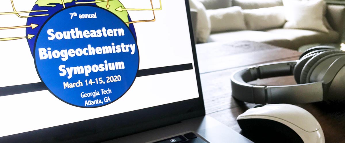Online conference setup for the Southeastern Biogeochemistry Symposium 2020 showing a laptop, headphones, and online slides